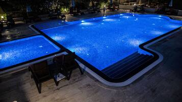 Una piscina amplia e iluminada con zona de solárium empavedada y sillones de descanso.