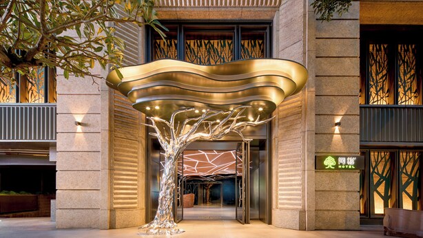 A modern hotel entrance with a unique tree-shaped light installation and a visible sign for the hotel. - arTree hotel (Taipei)