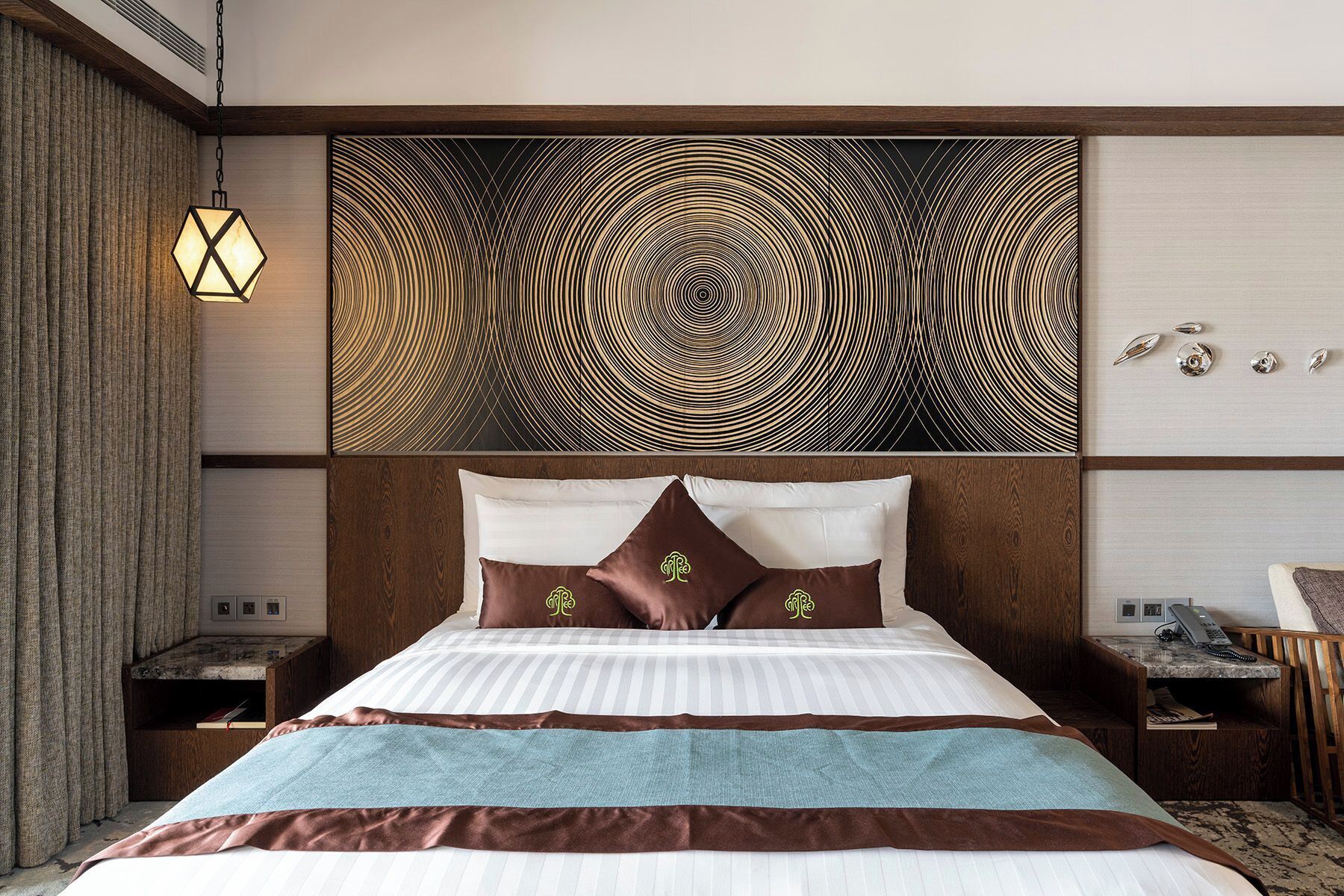 Habitación de hotel con una cama grande, cabecera de diseño circular y mesita de noche con lámpara.