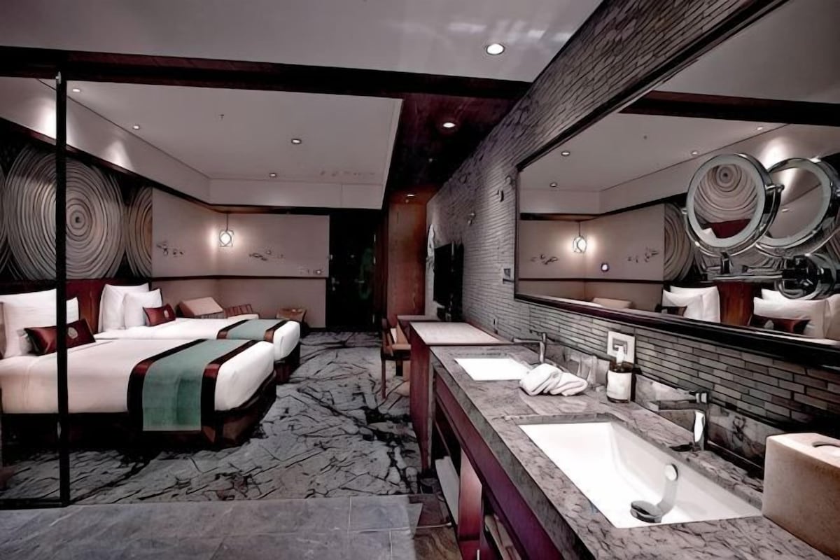 A hotel room with a large bed, two bedside tables, a long vanity with a mirror, and a marble floor.