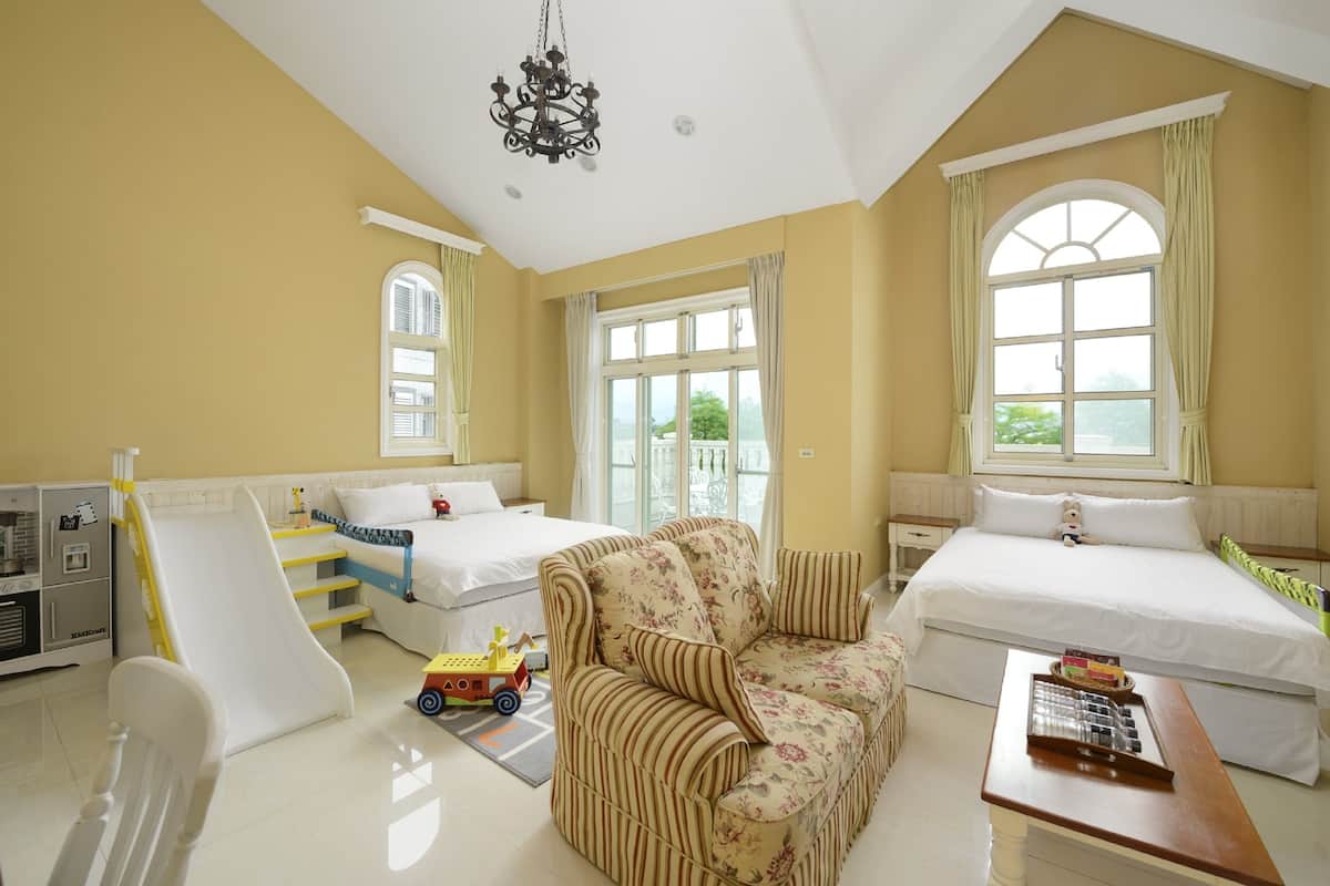 A room with two beds, a sofa, a desk, a chair, a toy train, and a chandelier.