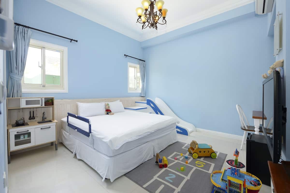 A bedroom with a bed, bedside table, and a play area with toys.