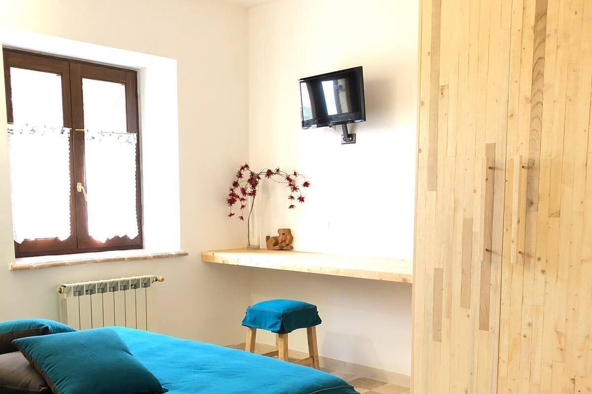 A bedroom with a bed, a window, a radiator, a TV, and a wardrobe.