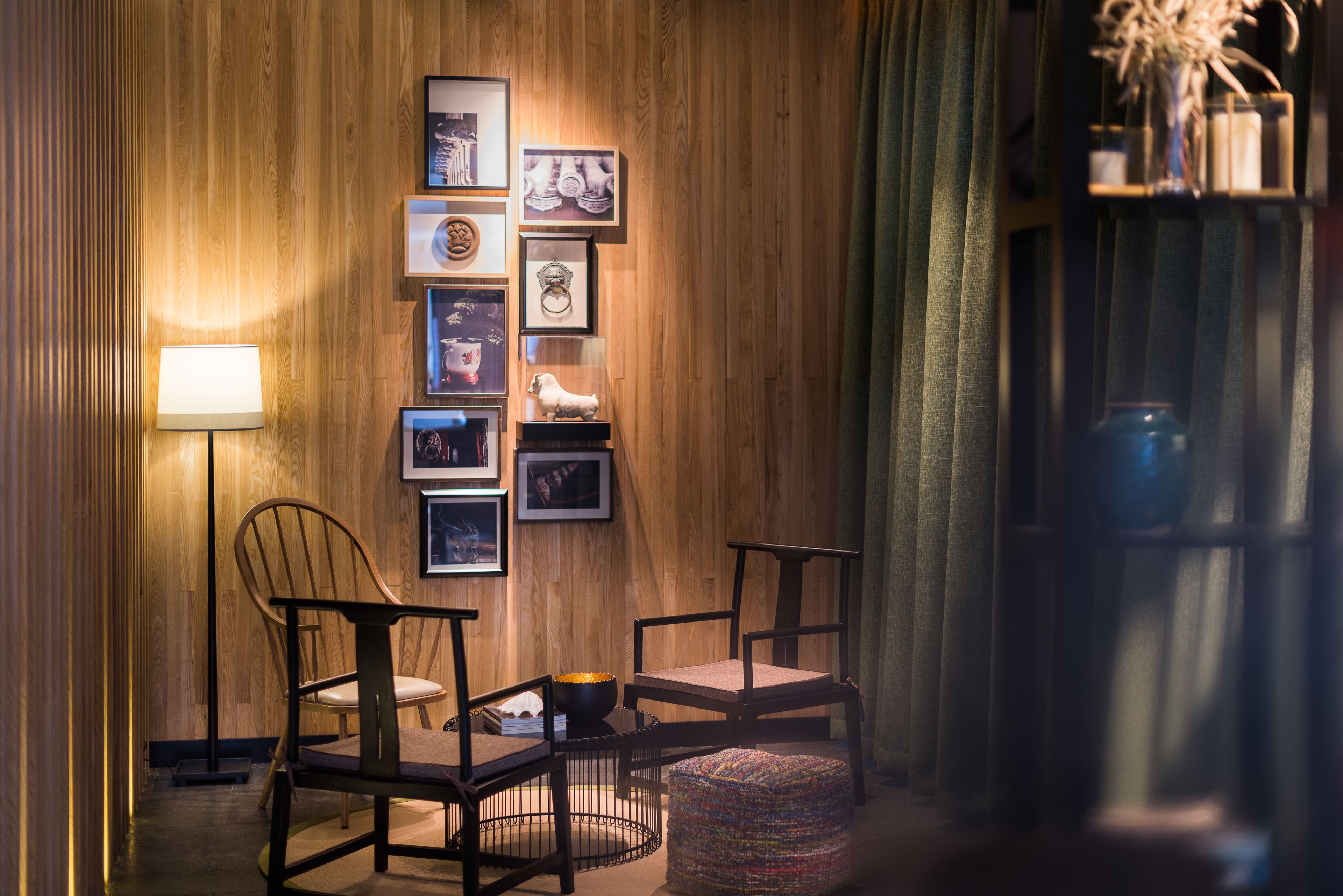 A cozy room with wooden paneling, a wall-mounted photo collage, two chairs, a small round ottoman, and a floor lamp.