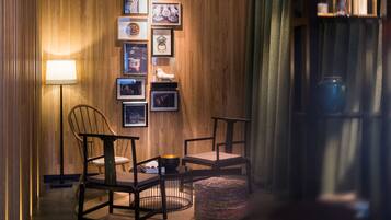 A cozy room with wooden paneling, a wall-mounted photo collage, two chairs, a small round ottoman, and a floor lamp.
