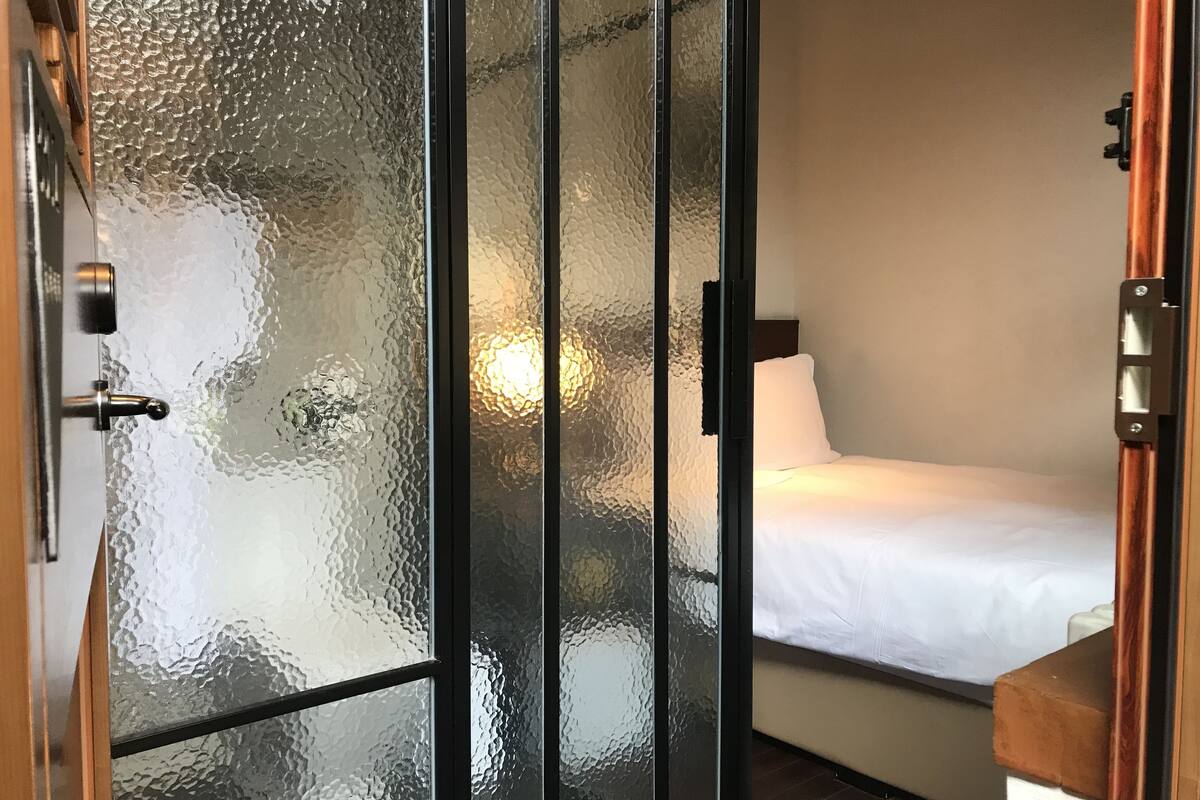 Habitació d'hotel amb un llit, una tauleta de nit i una porta de vidre mat.