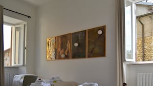 Une chambre d’hôtel avec un lit, une chaise, une table avec des serviettes et trois tableaux accrochés au mur.