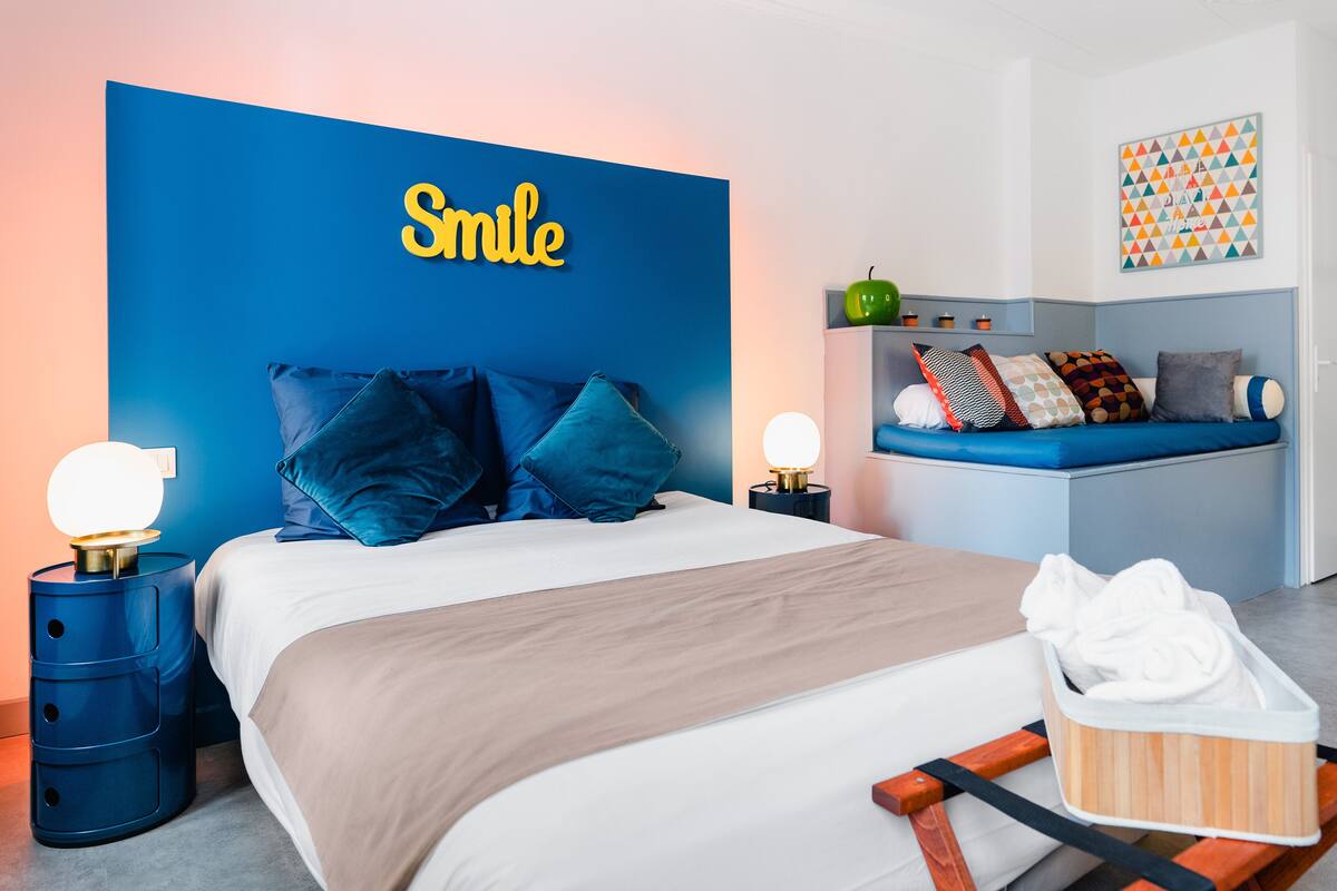 Una habitación de hotel moderna con una cama grande, un cabecero azul y un cartel en la pared que dice "Smile".