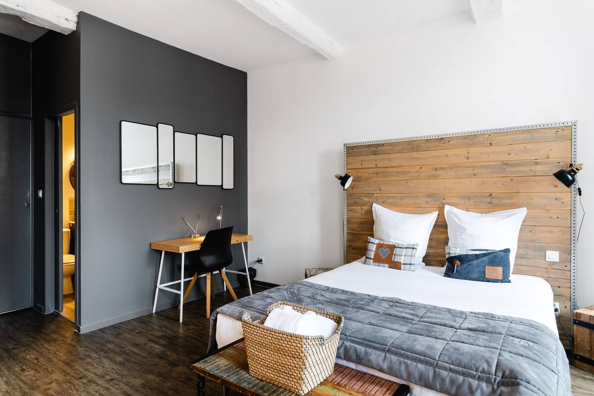 Un dormitorio moderno con cabecera de madera, un escritorio con silla y una cama grande con colcha gris.