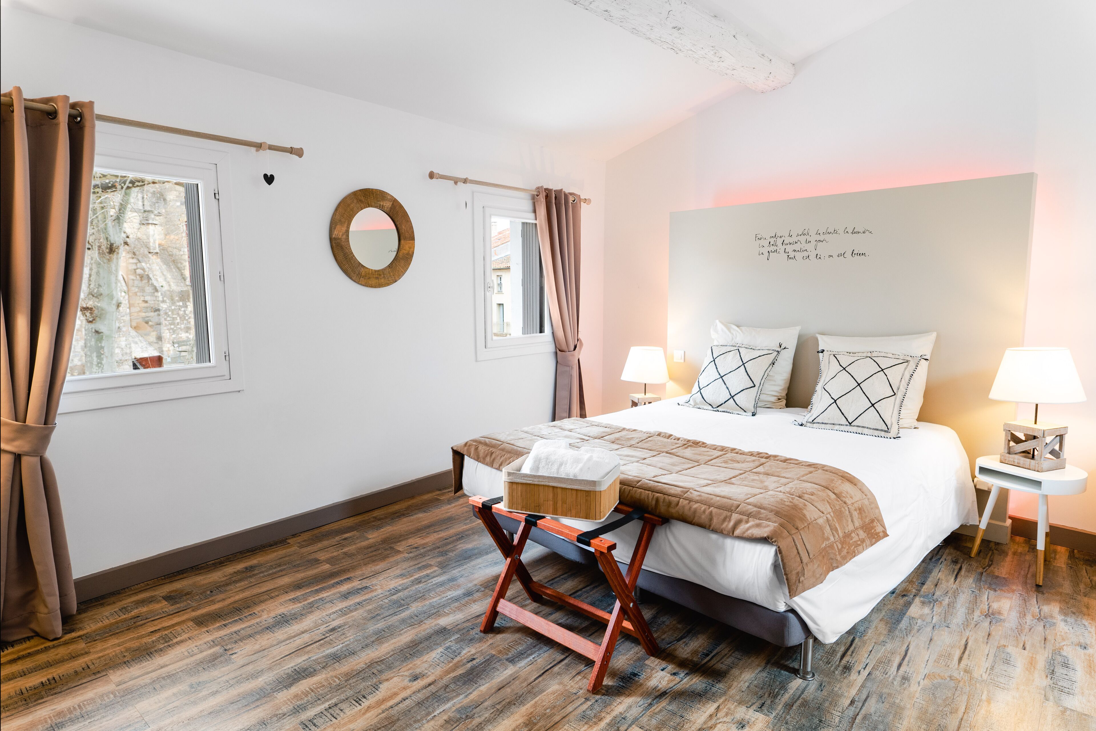 A bedroom with a bed, two bedside tables with lamps, a wooden floor, and a window with curtains.