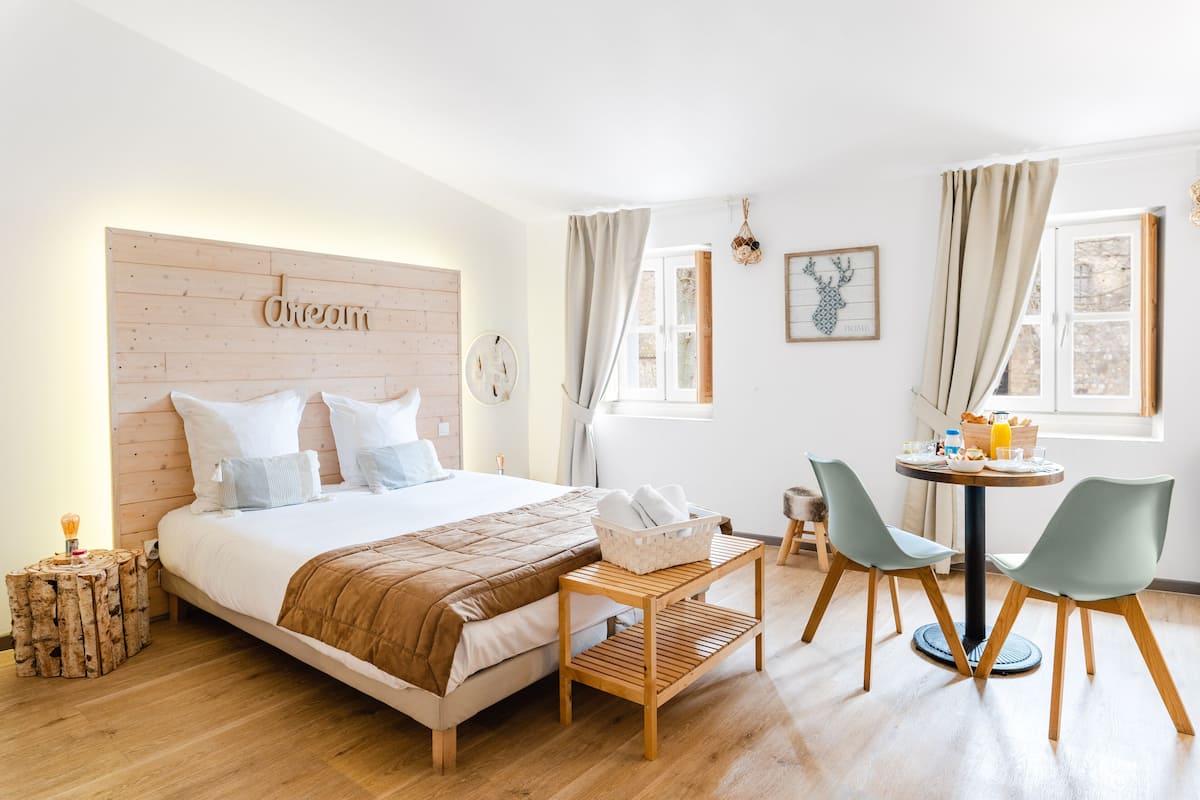 Un dormitorio con cabecera de madera, una cama con manta marrón, una pequeña mesa de madera con sillas y una mesa lista para el desayuno.