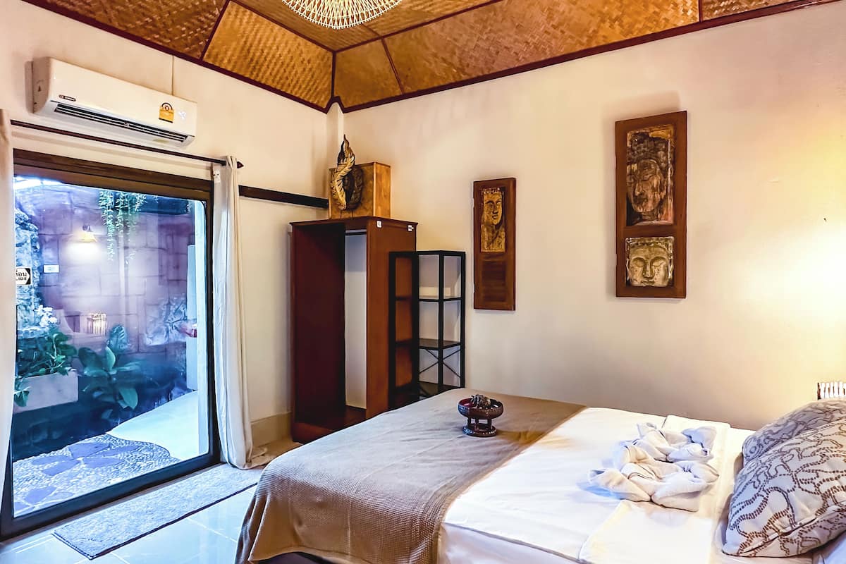 Quarto com cama, guarda-roupa, mesinha e janela com vista para um jardim.