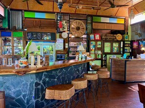 Un espace bar doté d’un comptoir en marbre, de tabourets en osier et d’un bureau d’accueil.