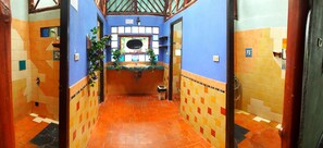 Un couloir étroit, dont le sol est recouvert de carreaux, mène à une salle de bain équipée d’un lavabo et d’un miroir.