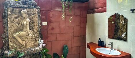 Un baño con un relieve de piedra, una planta colgante, un lavabo con espejo y paredes de azulejos.