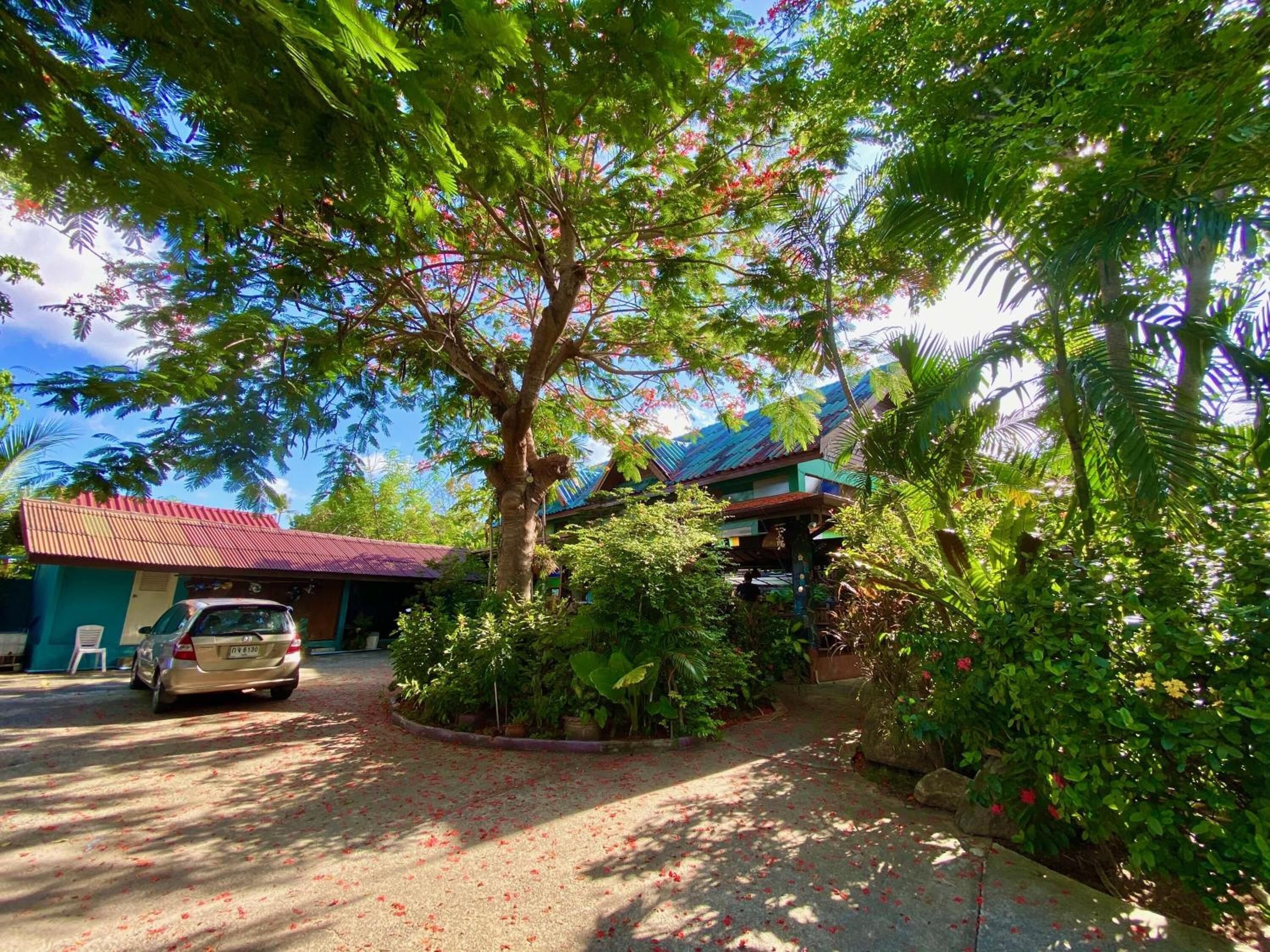 A building with a red roof, surrounded by lush greenery and a tree with red flowers.