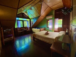 A cozy, triangular-roofed room with a bed, a desk, and a chair.