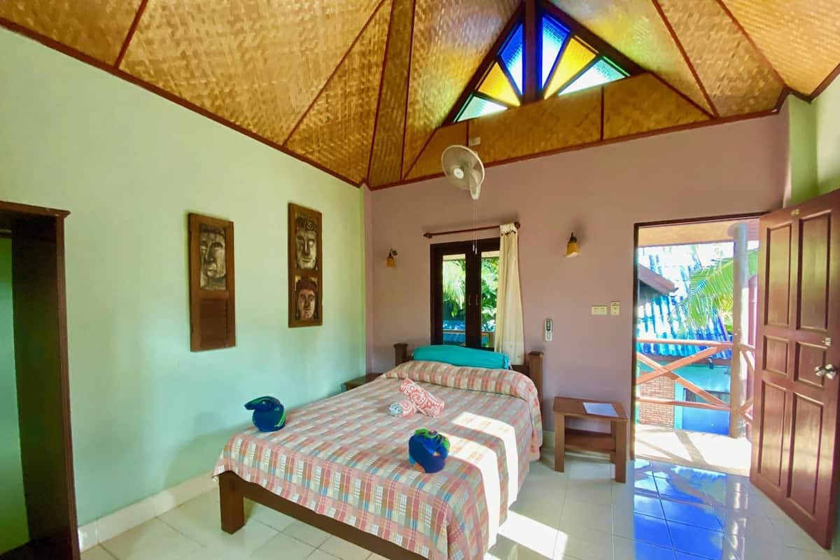 Quarto com duas camas, um ventilador e vista para uma escadaria externa.