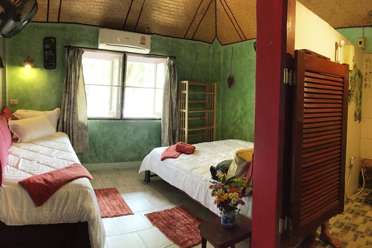 Een kleine, gezellige kamer met twee bedden, een raam, een houten trap en een badkamer zichtbaar door een open deur.