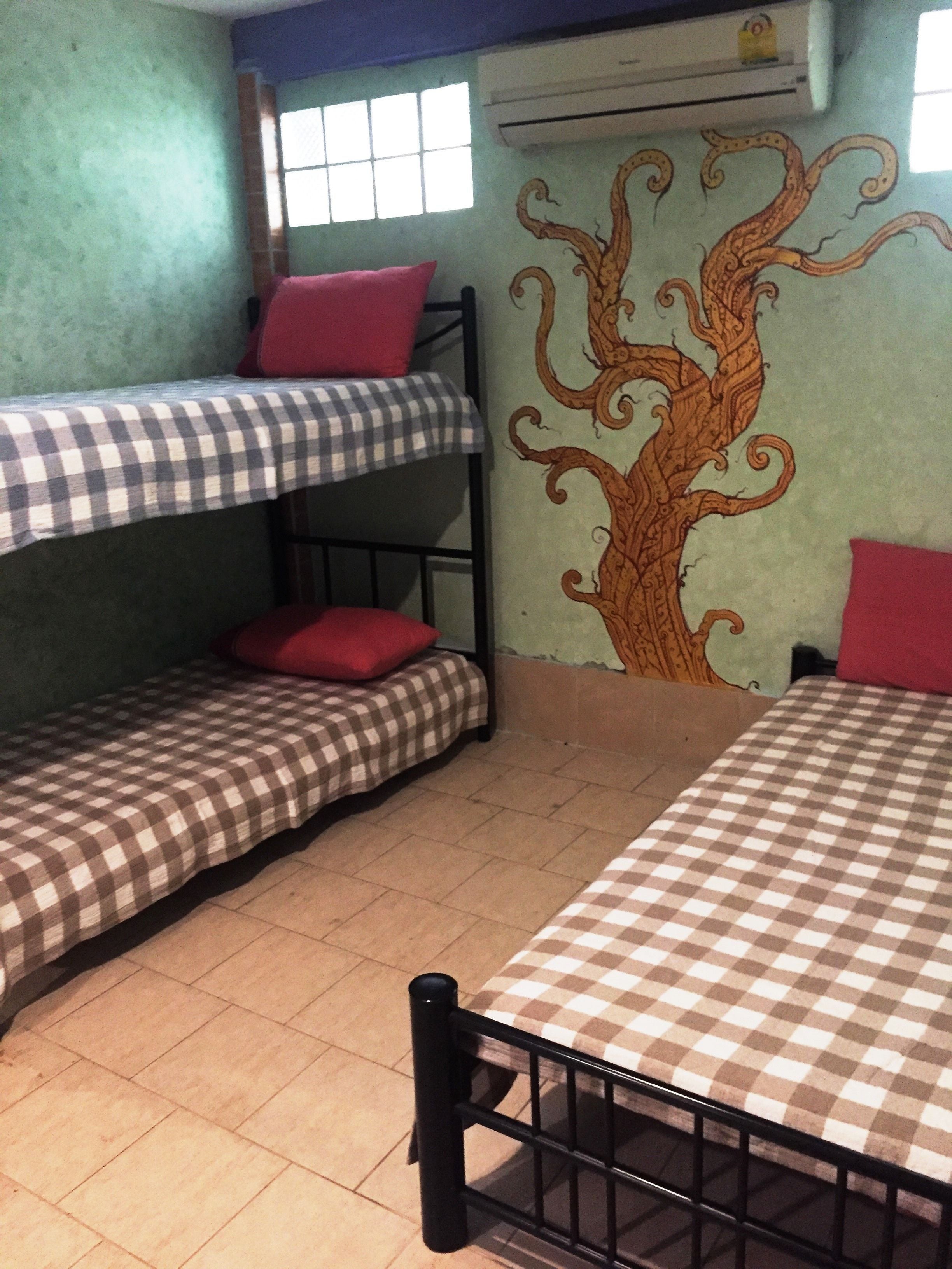 A dormitory room with bunk beds, a checkered bedspread, a wall mural, and an air conditioning unit.