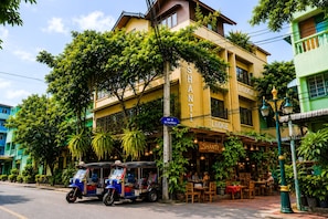 A building with a sign reading 'SHANTI LODGE' and a street in front with parked tuk-tuks.