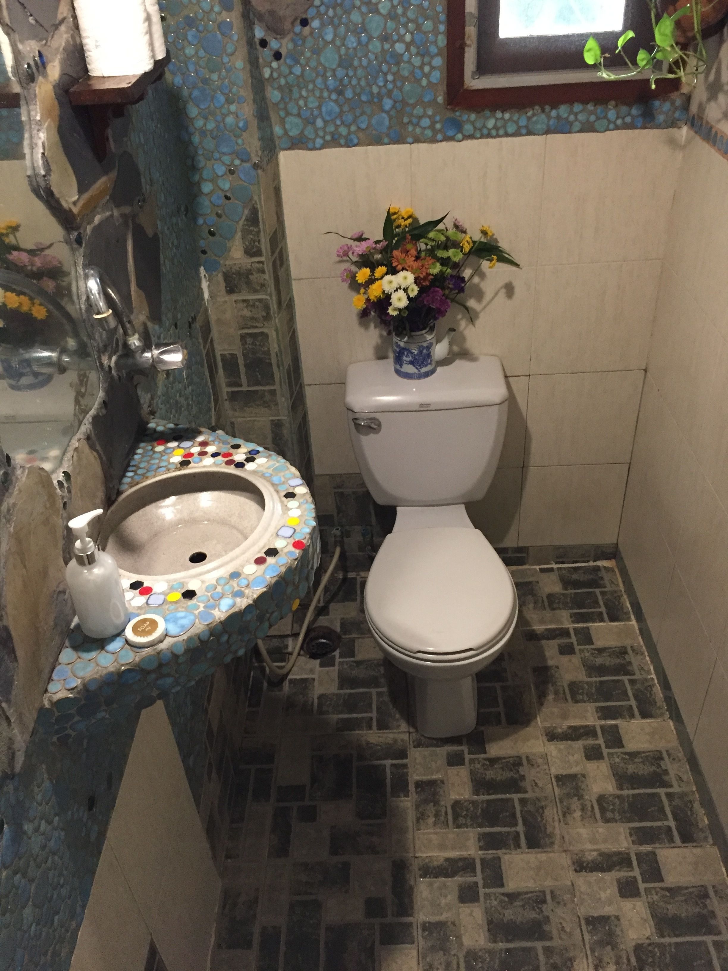 Un bagno con pavimento in mosaico, un water e un vaso di fiori, e un lavabo con dispenser di sapone.