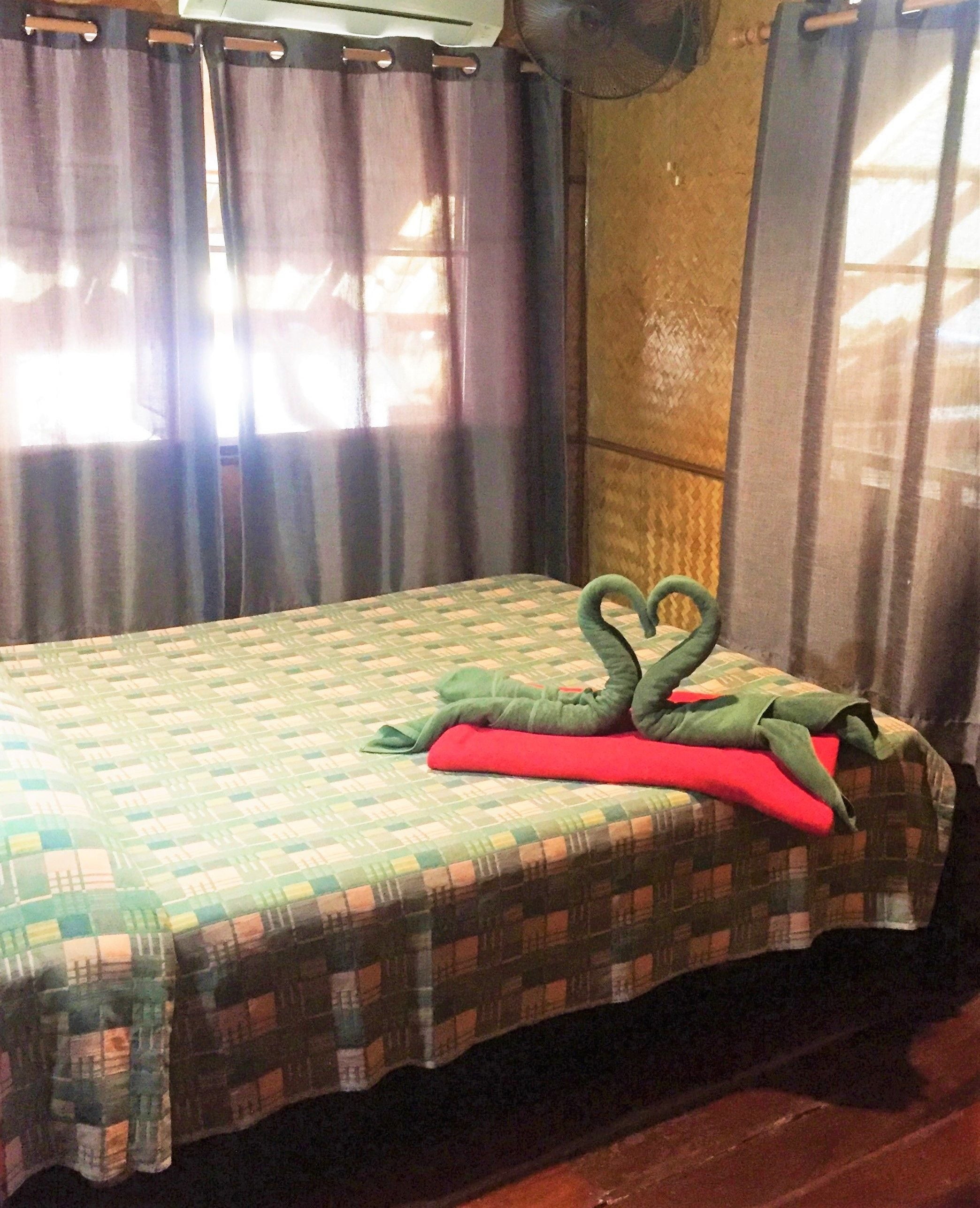 A single bed with a checkered bedspread, a green pillow, and a red pillow.