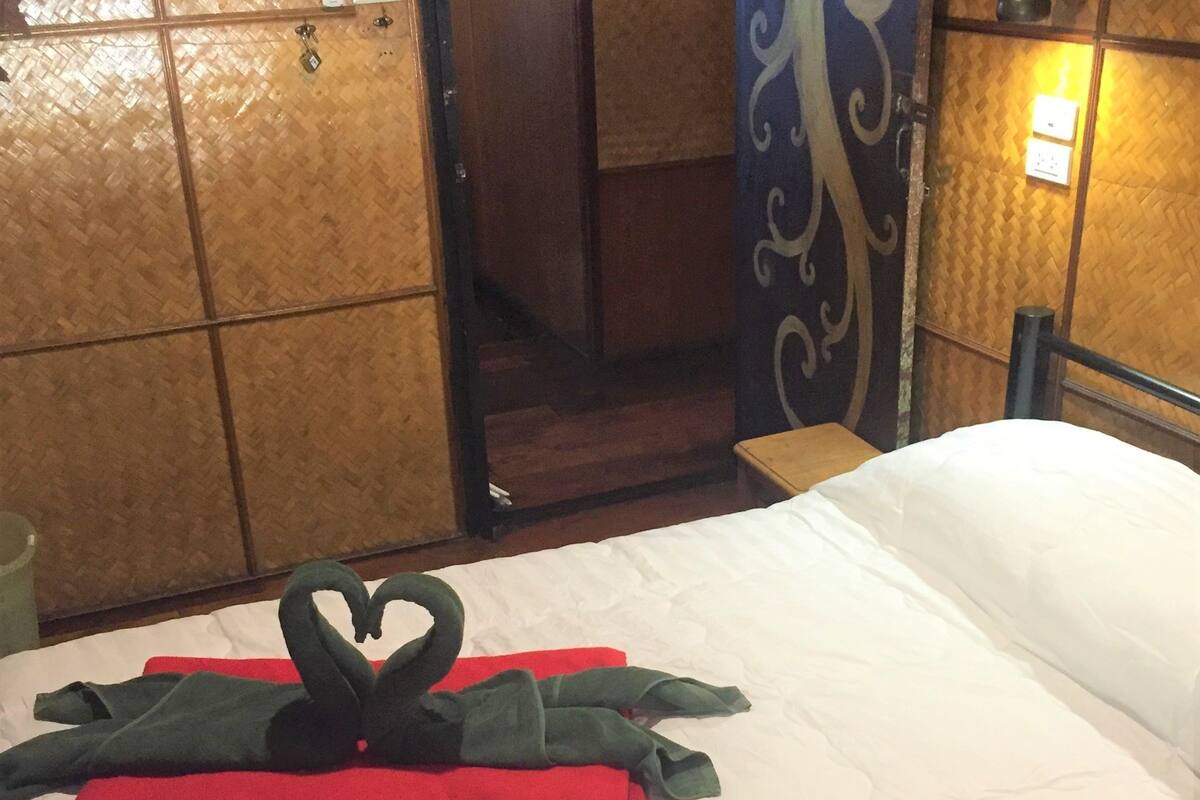 Een bed met een handdoekje in de vorm van een hart, een houten garderobe en een wandlamp.