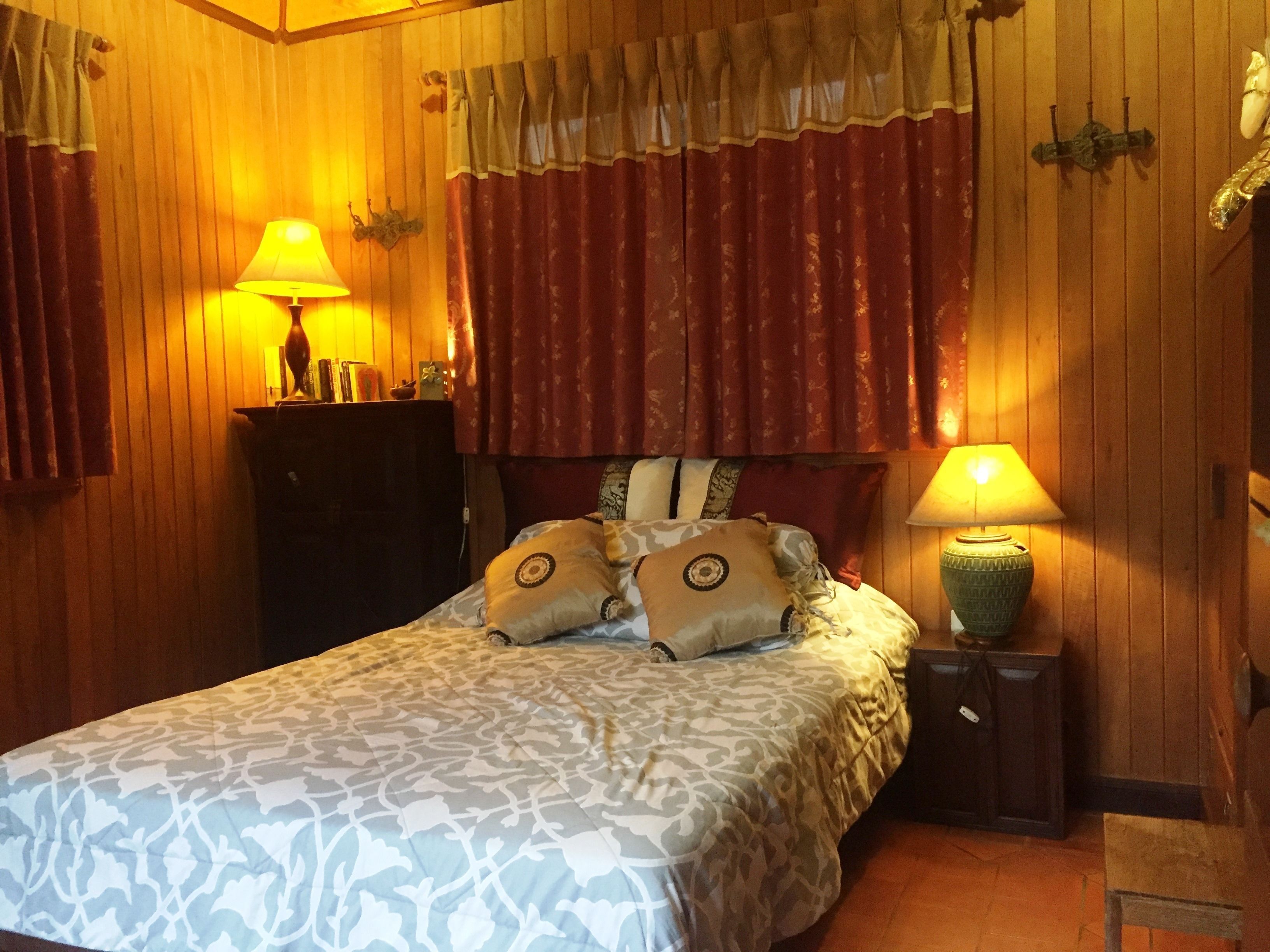 A room with a bed, two bedside tables, a wooden wardrobe, and a curtain.