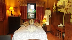 Une chambre bien éclairée, avec un lit, des oreillers, une table de chevet, une lampe, un peignoir, un miroir et une armoire.