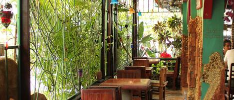 A restaurant with wooden tables and chairs, a stone floor, and a green wall with plants.