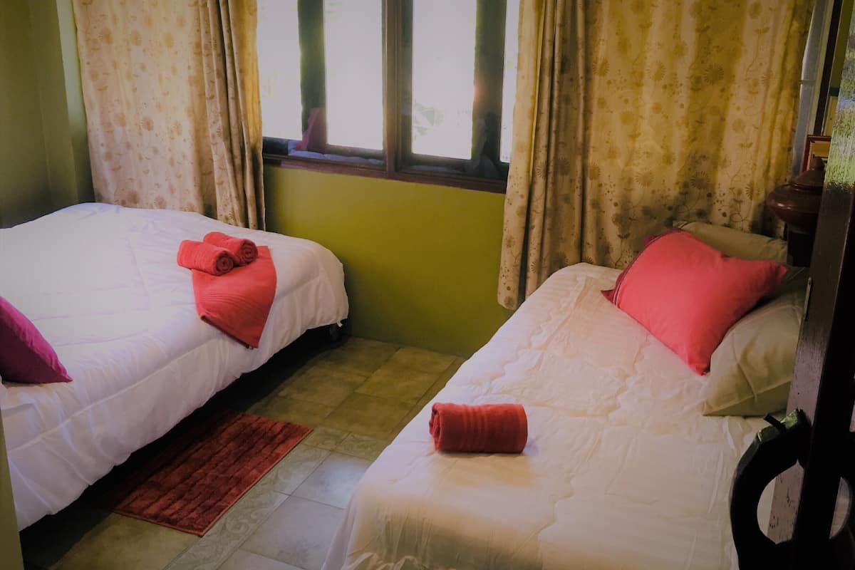 Een kamer met twee bedden, elk voorzien van een rode handdoek en een kussen. Er is een raam met gordijnen, en de muren zijn groen geverfd.