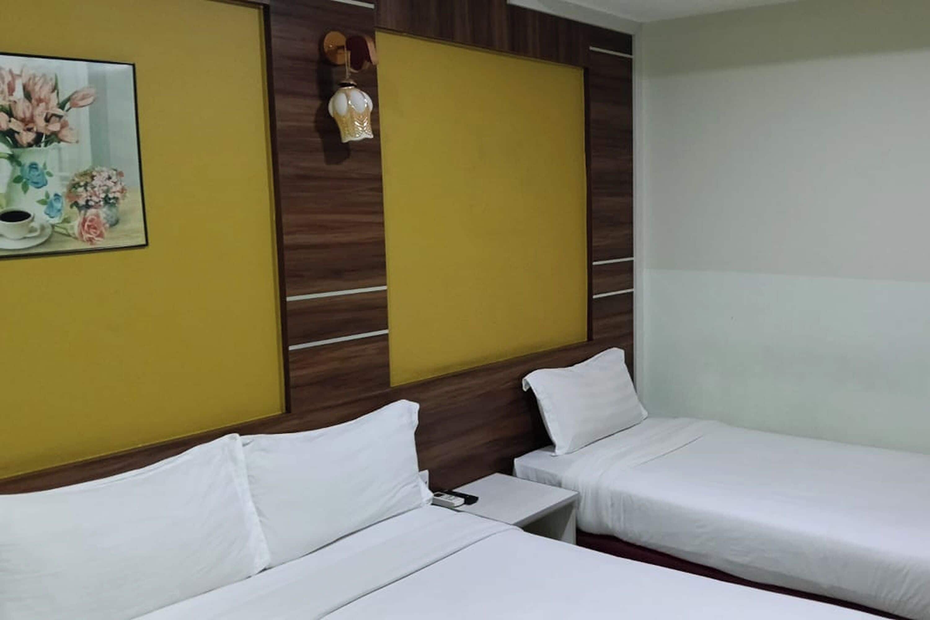 A hotel room with two single beds, a painting of flowers, a wall-mounted lamp, and a wooden accent wall.