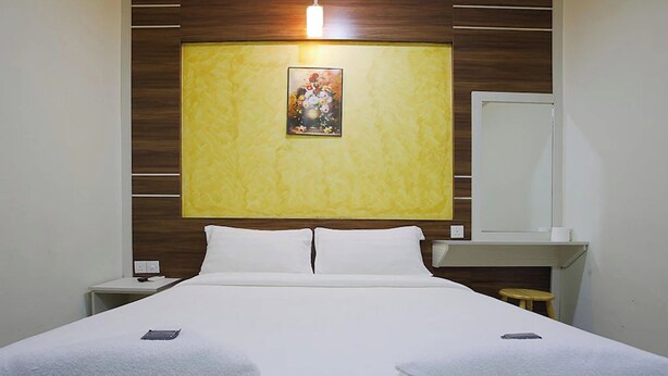 A hotel room with a bed, a nightstand, a bedside table, a mirror, and a wall-mounted artwork. - Golden Night Hotel Sunway (Subang Jaya)