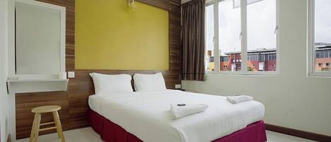 Habitación de hotel con cama, pared decorativa de madera, ventana con cortinas y vista a edificios.