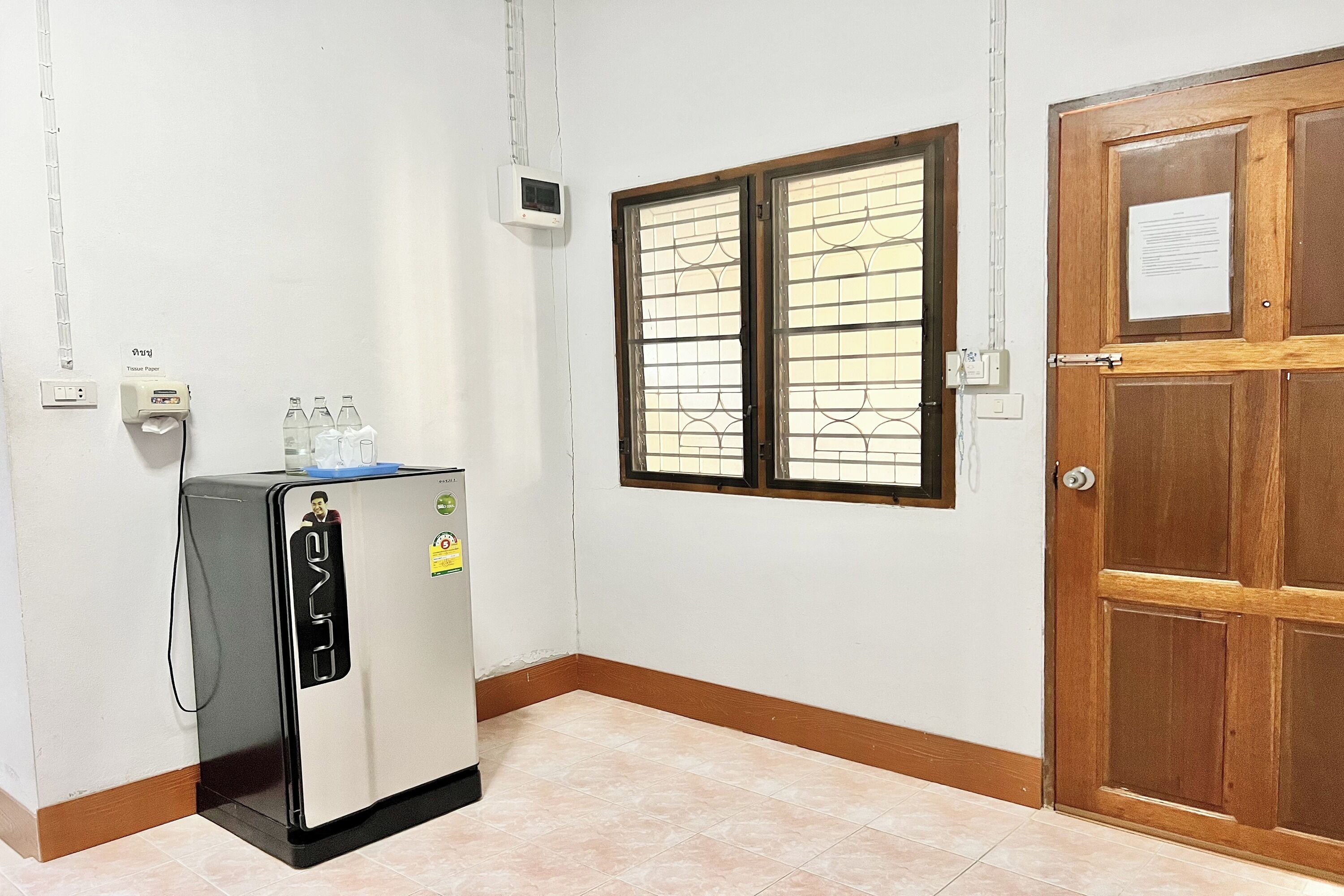 Cocina compacta con refrigerador, ventana con rejas, puerta de madera y aire acondicionado instalado en la pared.