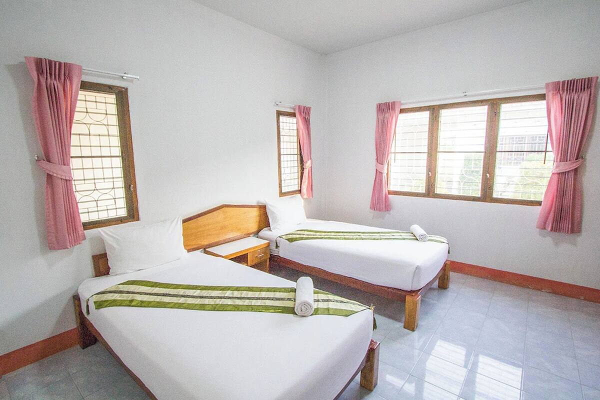 Una habitación con dos camas individuales, cabeceros de madera, ropa de cama blanca y cortinas rosas.