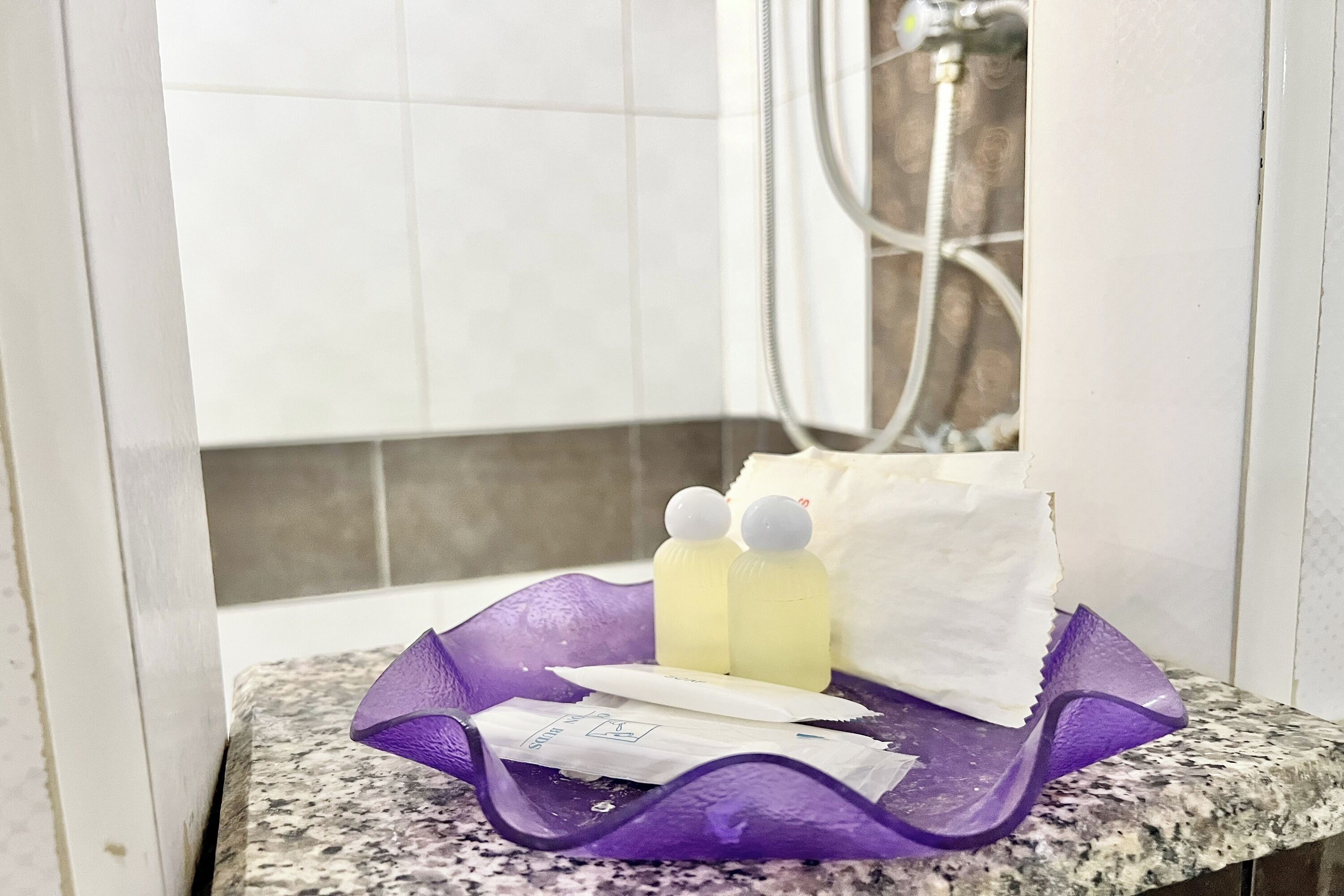A bathroom corner with a granite countertop, a purple soap dish, two bottles of liquid soap, a white towel, and a tissue box.