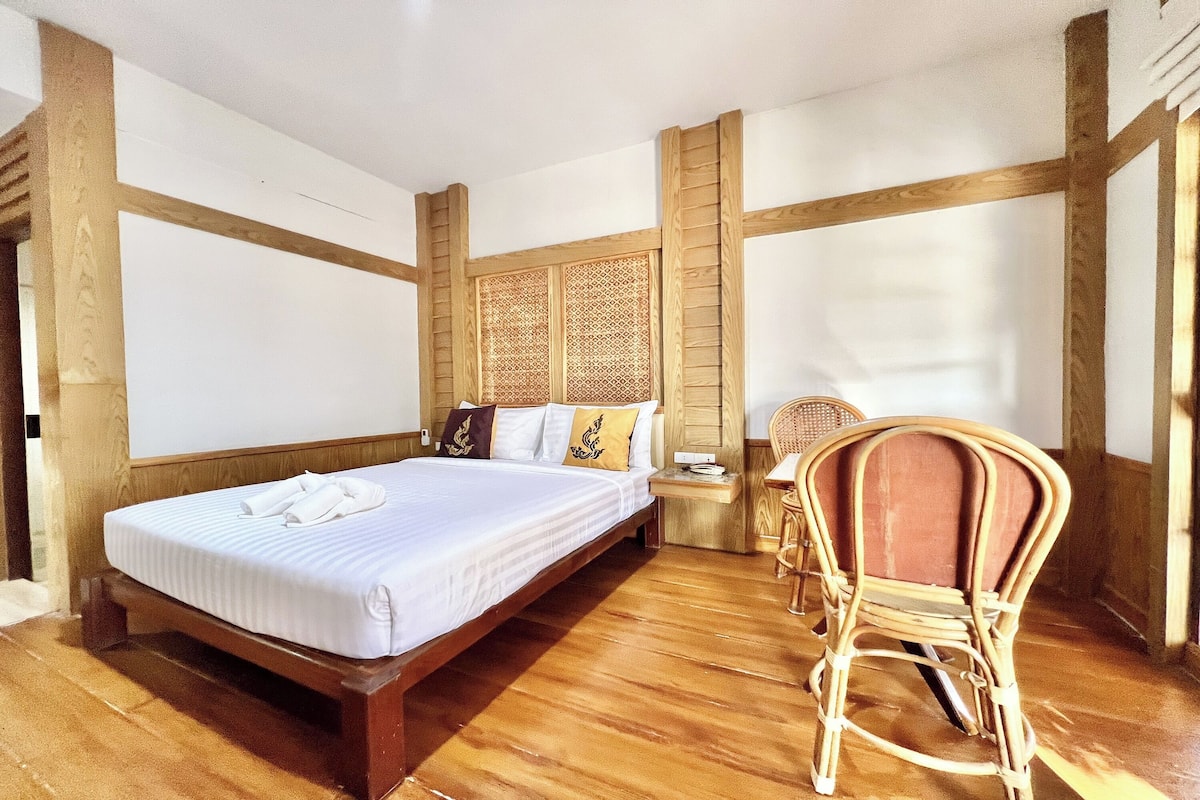 Un dormitorio con una cama de madera, una mesita de noche de madera, una silla de mimbre y un panel decorativo en la pared.