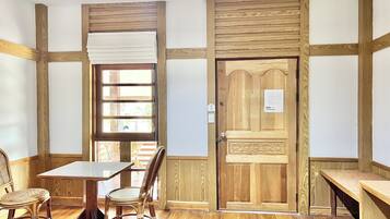 A room with a wooden table and chairs, a window with blinds, and a wooden door with a sign.