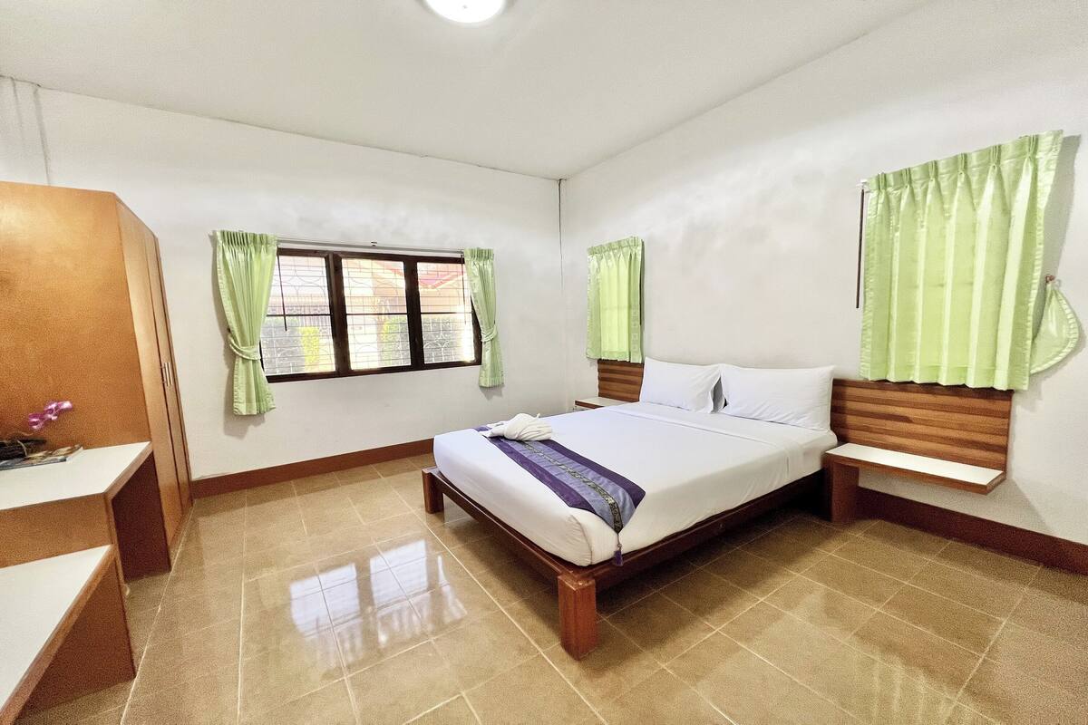 Un dormitorio con cama, mesita de noche, cortinas en la ventana y cabecero de madera.