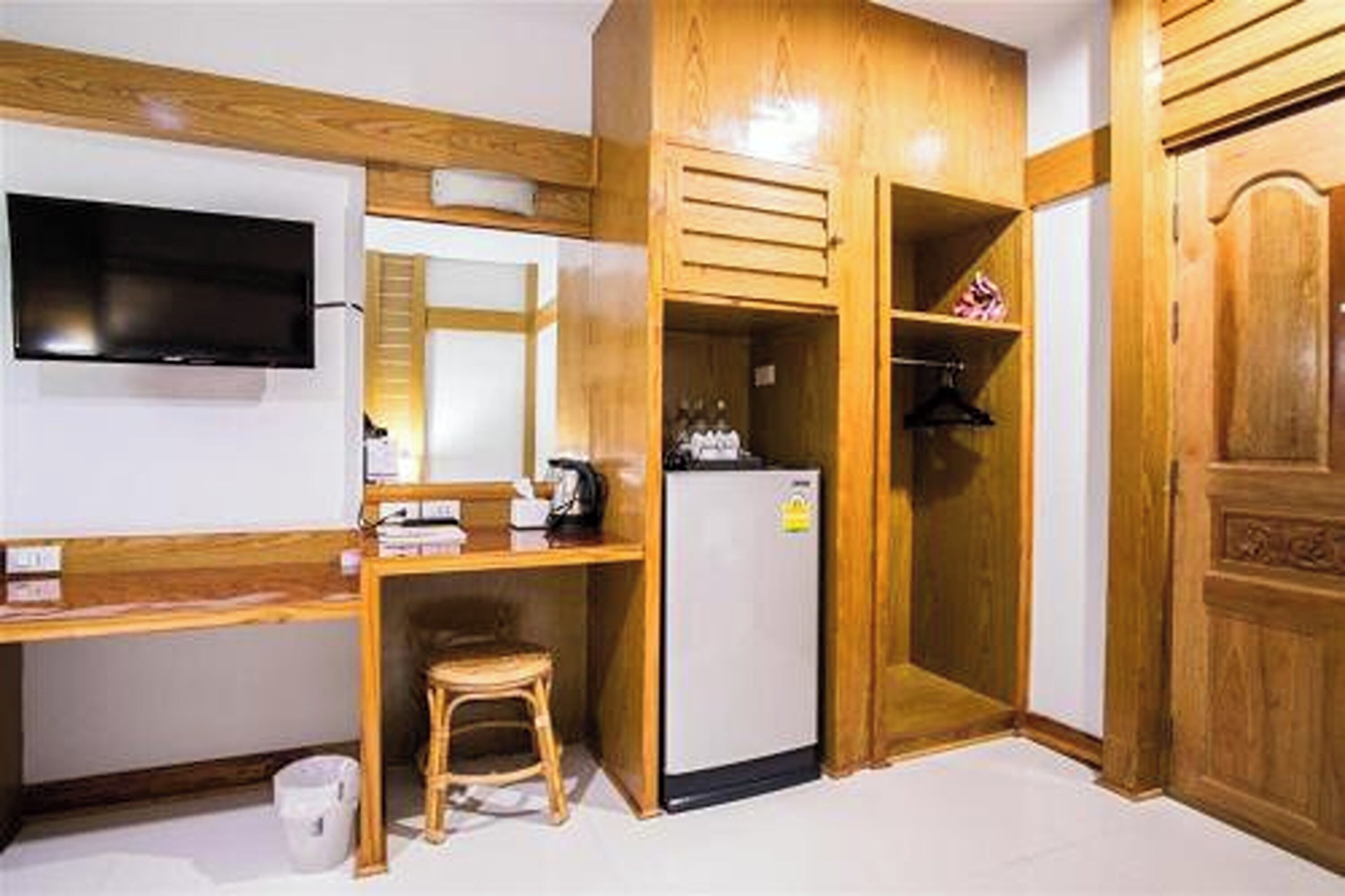 Una habitación compacta con escritorio de madera, televisor montado en la pared, refrigerador y armario.
