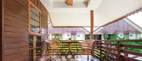 A wooden balcony with wicker chairs, a table, and a view of buildings and greenery.