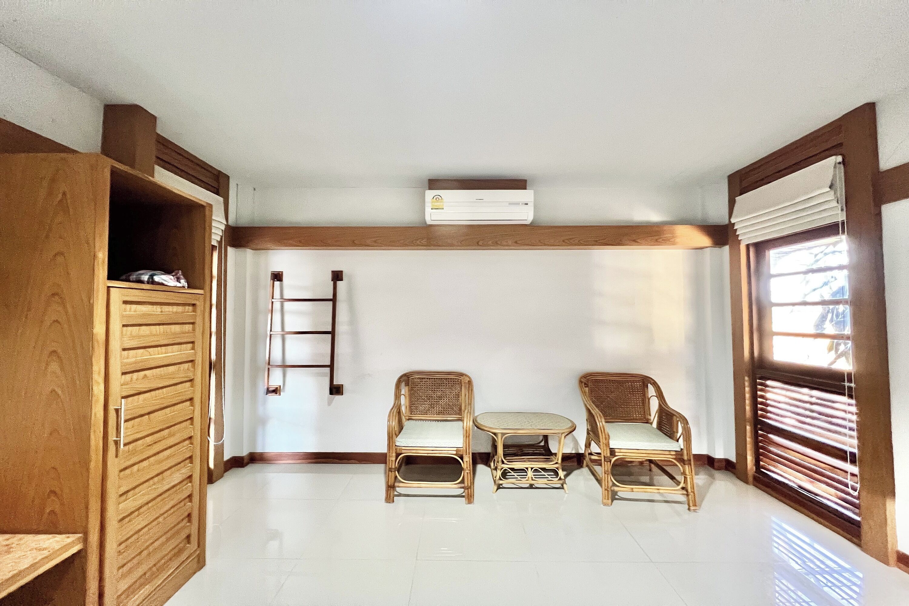 Una habitación con un armario de madera, dos sillas de mimbre, una mesita y una ventana con persianas.