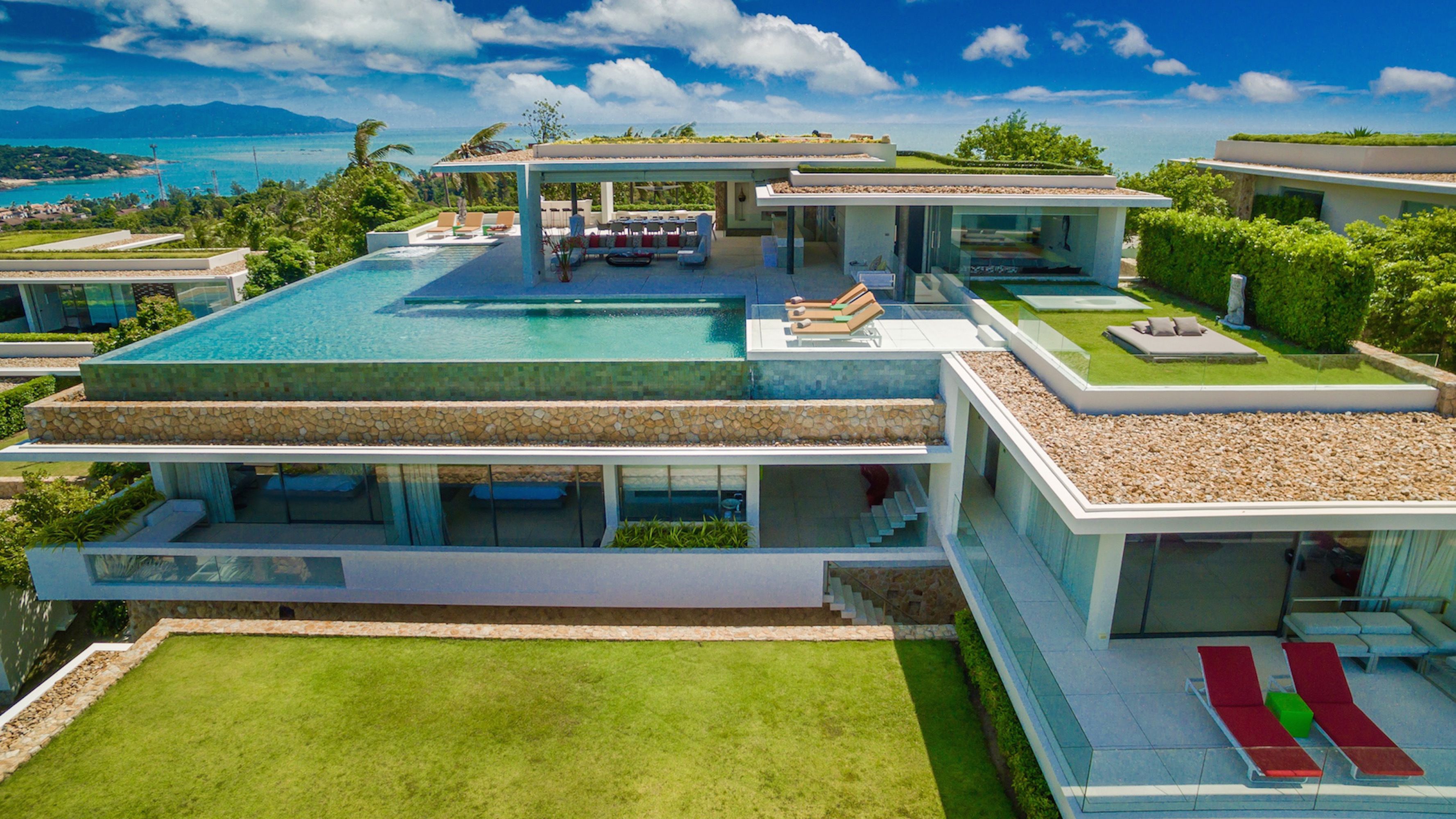 Uma casa moderna de vários andares com uma piscina grande, área de estar externa e vista para o oceano.