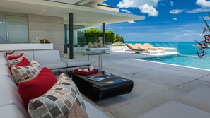 A modern outdoor living area with a pool, white sofas, and a glass wall overlooking the ocean. - Villa Anavaya (Koh Samui)