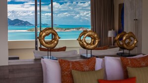 A hotel room with a large window offering a view of a turquoise sea and distant mountains. There are three golden rings displayed on the windowsill. - Villa Anavaya (Koh Samui)