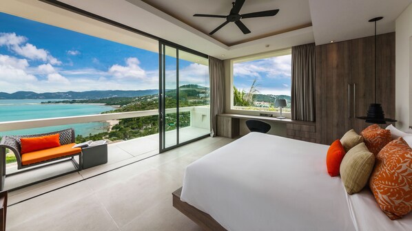 A modern hotel room with a large bed, a balcony with a view of the sea, and a desk with a chair.