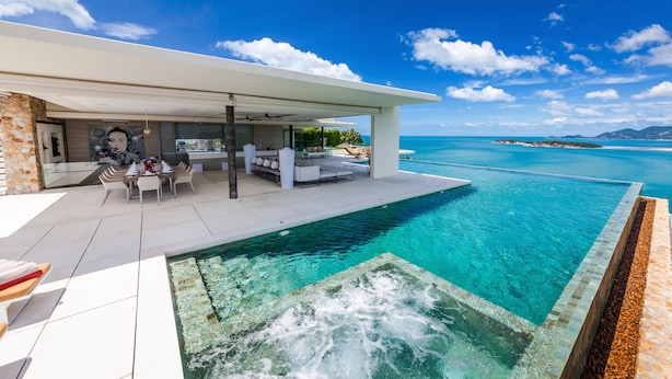 A modern infinity pool with a clear view of the ocean, a covered outdoor seating area, and a stone facade. - Villa Anavaya (Koh Samui)