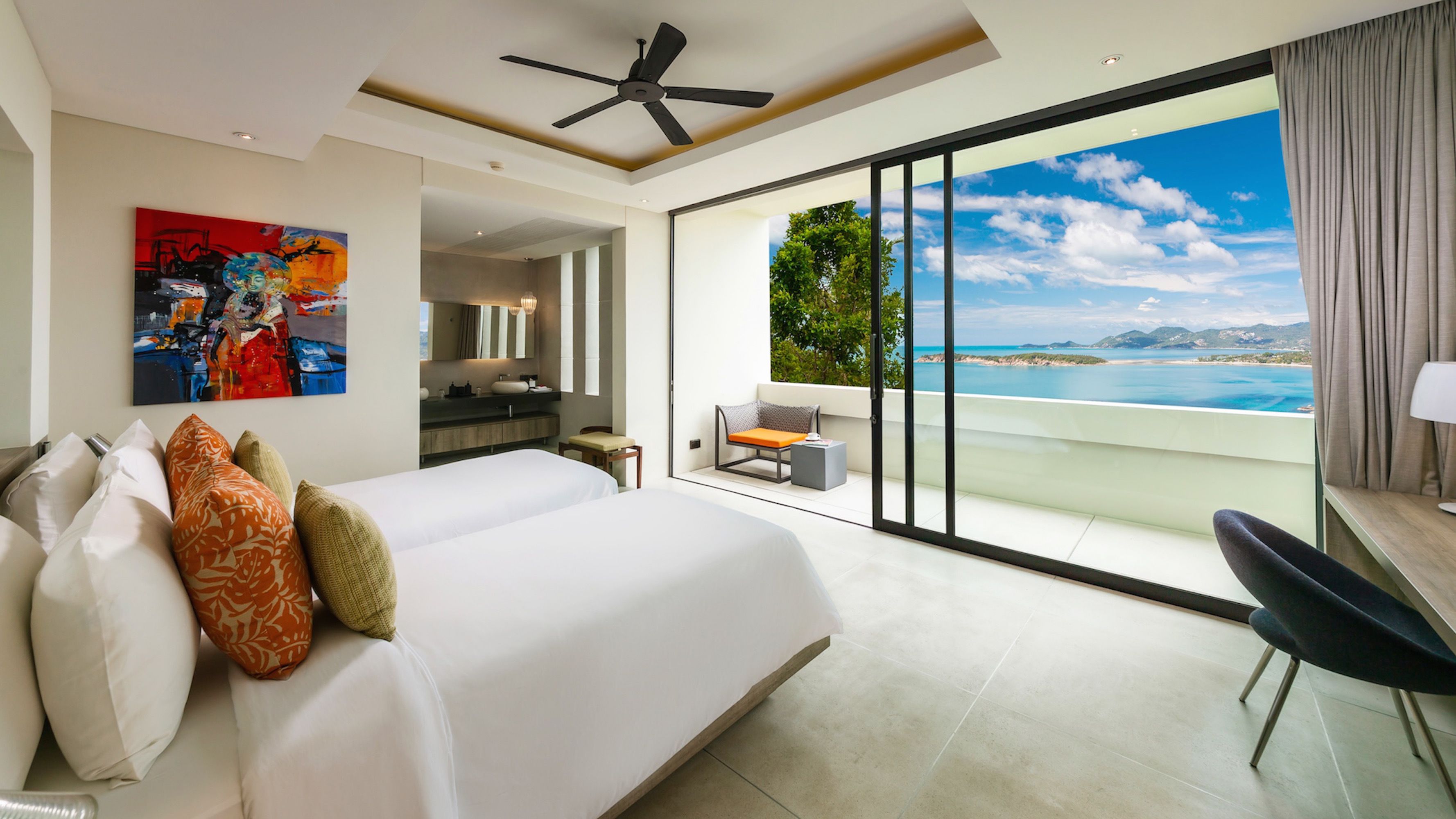 A modern hotel room with a large bed, a desk, and a balcony with a sea view.